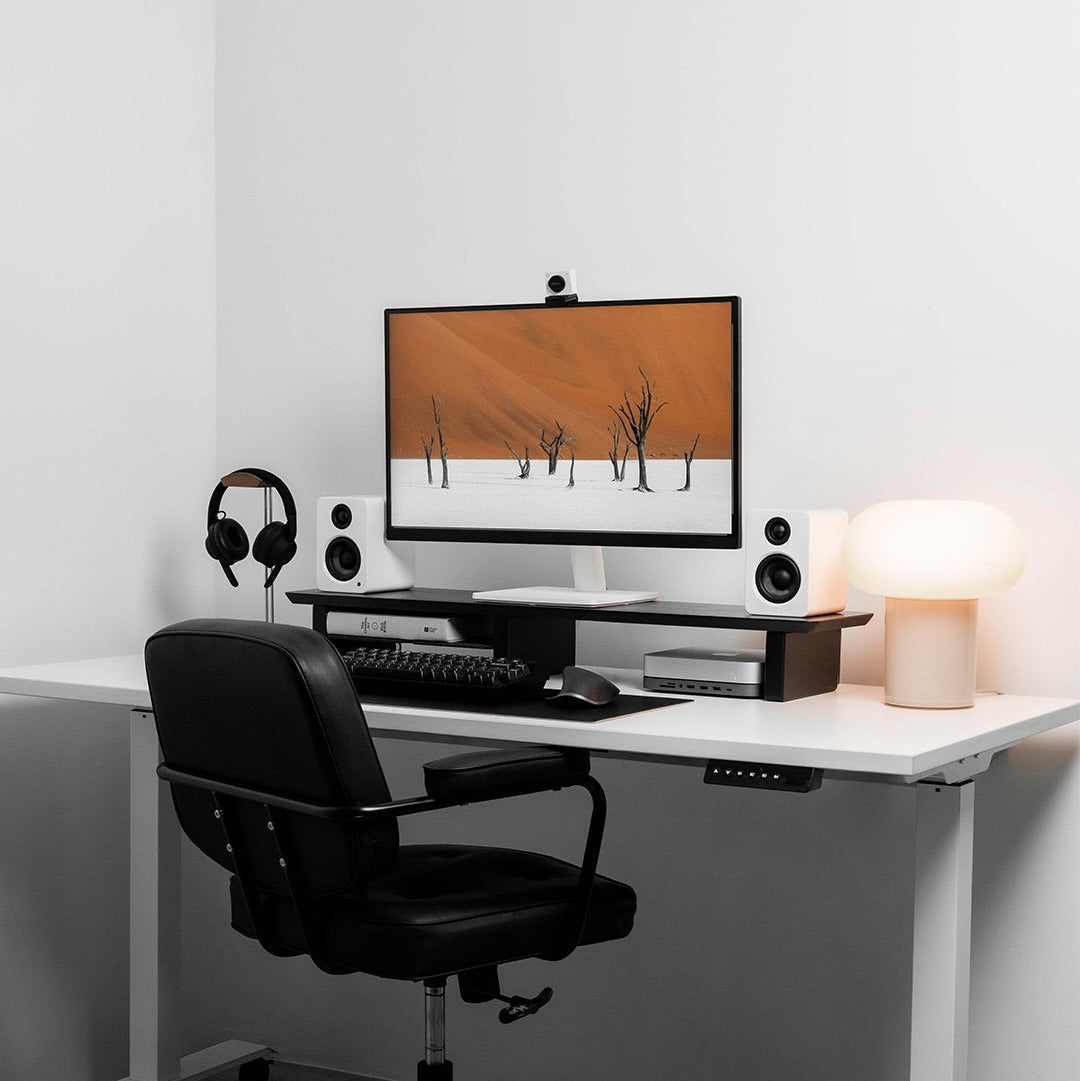 Modern home office setup with a desk, computer monitor, keyboard, mouse, headphones, speakers, and a lamp.