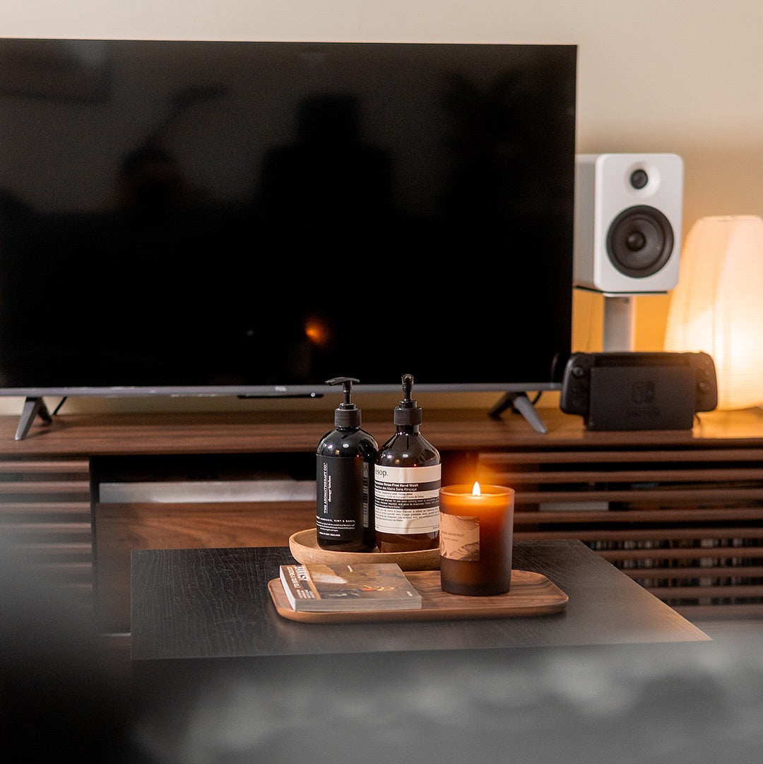 Bottles on a wooden tray with a candle in front of a television and speakers.